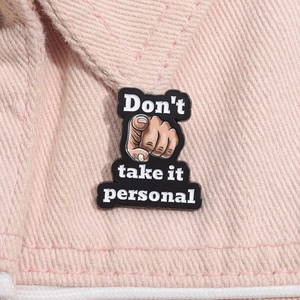 Close-up of black enamel finger brooch with Don't take it personal text on denim