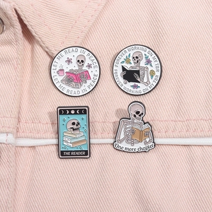 Close-up of four skull and book enamel pins on a pink denim background detail