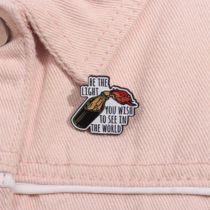 Macro detail of enamel pin showing Molotov bottle with Be the Light quote text