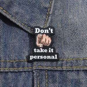 Close-up of 'Don't take it personal' enamel pin on a blue denim jacket collar