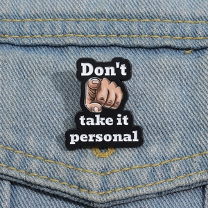 Detail view of an enamel pin with 'Don't take it personal' text on denim fabric