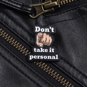 Detail of an enamel brooch on a black leather jacket with the text Don't take it personal