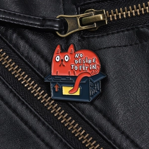 Macro shot of cat enamel pin in blue box on leather jacket with text NO DESIRE TO FIT IN