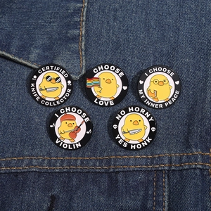 Macro detail of five cartoon duck enamel pins with various motifs on blue denim fabric