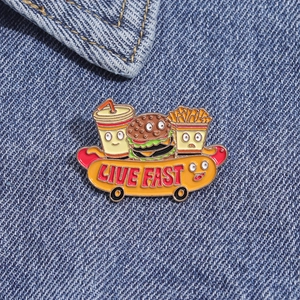 Détail du pin's émaillé burger et frites dessin animé sur tissu en jean bleu