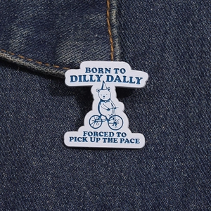 Macro view of a bear riding a bike enamel pin on denim with funny lettered slogans