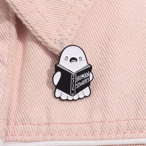 Close-up of ghost reading Human Stories book enamel pin on pink denim fabric