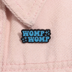 Dettaglio della spilla smaltata WOMP WOMP blu sul colletto di una giacca di jeans rosa