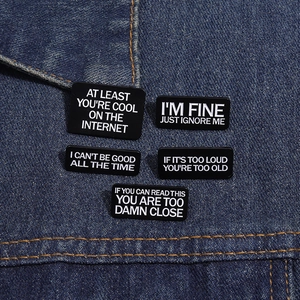 Détail de cinq pin's en émail noir avec slogans blancs sur tissu en denim bleu foncé