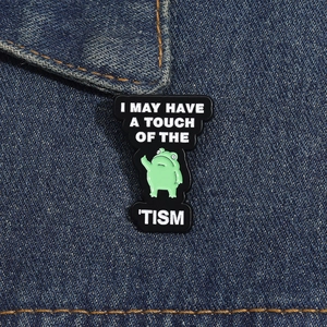 Close-up of a funny green frog enamel pin on denim jacket with humorous text engraving