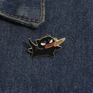 Gros plan d'un pin's chat noir émaillé avec couteau crime sur tissu denim