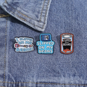 Macro shot of three funny blue bean can enamel pins set on dark denim fabric background