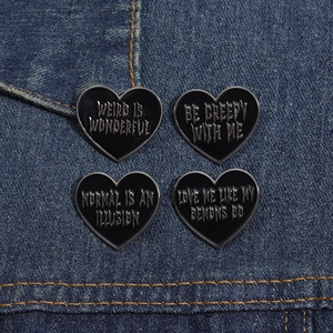 Set of four black heart enamel pins with gothic slogans on a denim fabric background