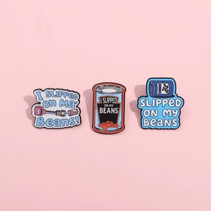 Three cartoon enamel pins featuring I Slipped On My Beans humor on a pink background