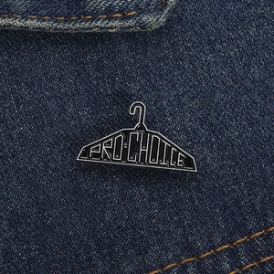 Dettaglio della spilla a forma di gruccia in smalto nero con scritta Pro-Choice su denim