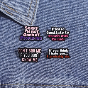Détail de quatre broches en émail noir avec citations humoristiques sur denim bleu