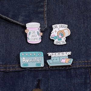 Macro shot of mental health enamel pins including Lexapro bottle and therapy sofa on denim