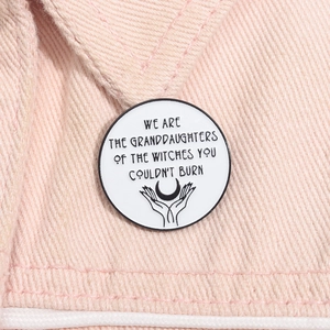Macro view of a white enamel feminist badge pinned on pink denim with moon graphic