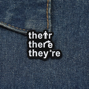 Detail of black enamel grammar brooch showing their there they're on denim jacket