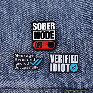 Close-up of funny enamel pins with SOBER MODE OFF text on dark blue denim fabric
