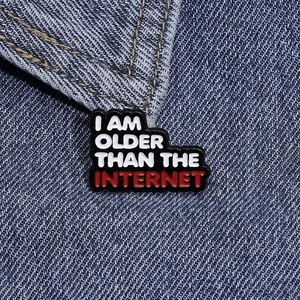 Macro shot of a black enamel pin with I Am Older Than The Internet text on denim