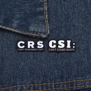 Detail of CRS and CSI enamel pins featuring funny acronyms on dark denim fabric