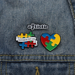 Macro shot of three autism awareness enamel pins on blue denim, featuring puzzle heart designs
