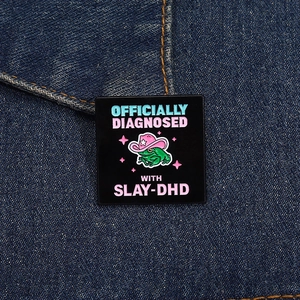 Detail of square black enamel pin featuring a frog in a pink cowboy hat on denim fabric