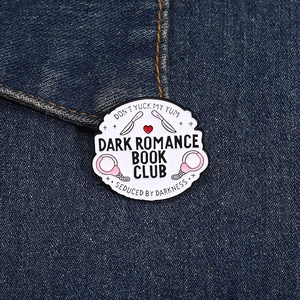Gros plan sur le pin's Dark Romance Book Club avec poignard et menottes sur denim