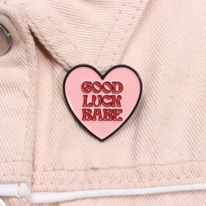 Close-up of Good Luck Babe pink heart enamel pin on light pink denim fabric texture