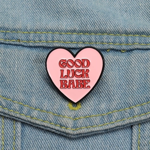 Détail d'un pin's en émail cœur rose avec texte Good Luck Babe sur veste en jean