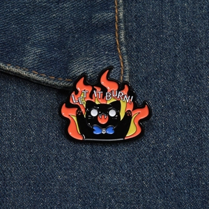 Detailed enamel cat badge with Let It Burn text on blue denim fabric background