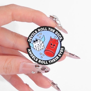 Enamel pin with red capsule and winged dice featuring 'Devils Roll The Dice' quote