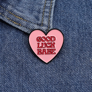 Close-up of pink heart enamel pin with Good Luck Babe text on blue denim jacket