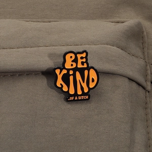 Macro shot of an orange enamel pin with ironic quote on a brown canvas backpack