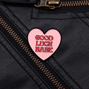 Detailed macro of pink heart enamel pin with Good Luck Babe text on black leather jacket