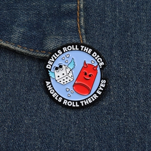 Detail of enamel pin with dice and devil characters pinned on blue denim fabric