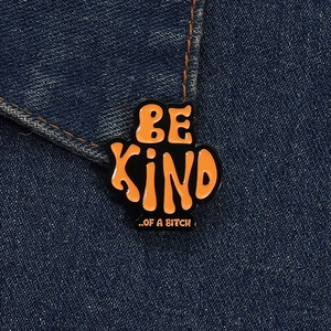 Close-up of funny enamel pin with orange text saying BE KIND OF A BITCH on denim jacket