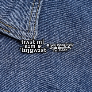 Detailed view of two linguistic humor enamel pins displayed on blue denim fabric background
