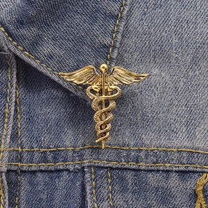 Detail view of a vintage gold Caduceus brooch with twin snakes on a blue denim jacket lapel