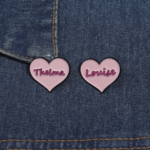 Close-up of pink heart-shaped Thelma and Louise enamel pins on blue denim fabric