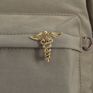 Detailed close-up of golden Caduceus snake brooch pinned to a green tactical bag