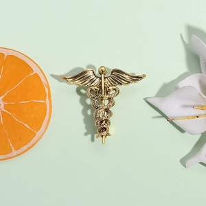 Golden Caduceus snake brooch with wings in vintage relief style on light green base