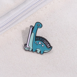 Detail of blue enamel dinosaur pin with Herbivore text on white canvas background