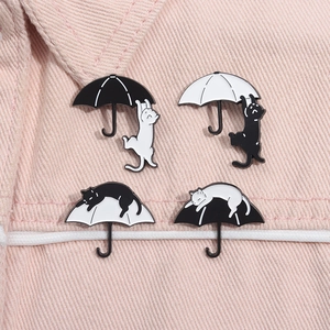 Detailansicht von vier schwarz-weißen Katzen-Regenschirm-Anstecknadeln auf rosa Denim
