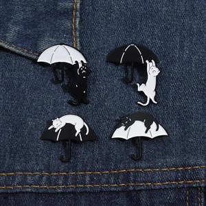 Set mit vier Emaille-Pins mit Katzen- und Regenschirmmotiven auf Denim-Hintergrund