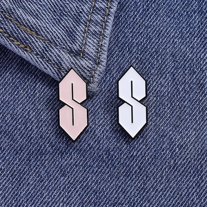Close-up of pink and white 'Cool S' enamel pins on dark blue denim fabric texture