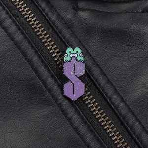 Détail macro d'un pin's grenouille verte sur un badge S violet pailleté sur une veste cuir