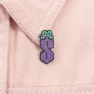 Détail macro du pin's émaillé Cool S avec grenouille verte sur fond de denim rose pâle