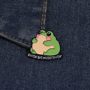 Detail of cute green frog enamel pin with funny quote on dark denim fabric texture